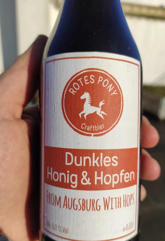 Eine Hand hält eine Flasche vom Dunklen Honig & Hopfen der Rotes Pony Craft-Beer-Brauerei